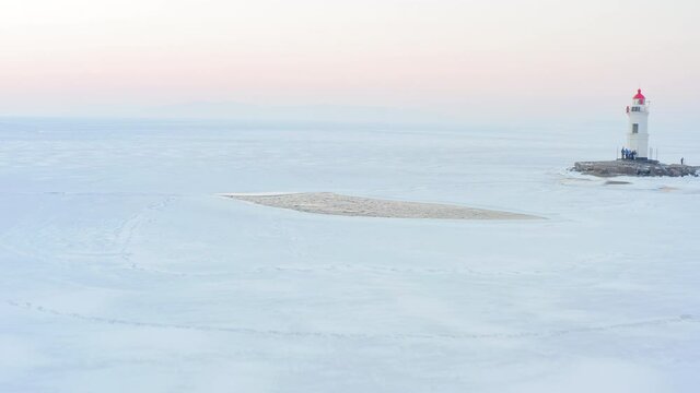 Flight over the frozen sea and drone view of Tokarevsky lighthouse at dawn