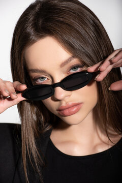 close up view of young brunette woman looking at camera over black sunglasses isolated on grey.
