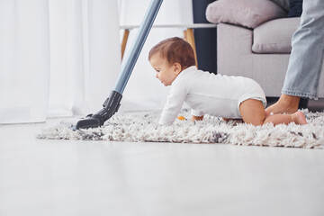 Using of the vacuum cleaner. Mother with her little daughter is indoors at home together