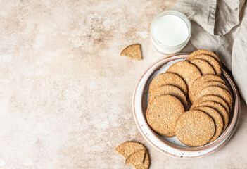Tasty crackers with seeds on a plate and cup of milk, brown background. Snack or breakfast. Top view.