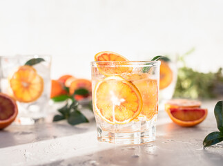Tonic nonalcoholic mocktail with red Sicilian oranges and ice, grey background. Cold refreshing summer mojito lemonade. Direct sunlight and hard shadows.