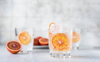 Tonic nonalcoholic mocktail with red Sicilian oranges and ice, grey background. Cold refreshing summer mojito lemonade.