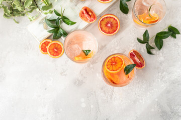 Cold refreshing drink with tonic, blood Sicilian oranges and ice, grey background. Cocktail with...