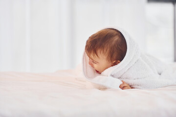 With white towel. Cute little baby is indoors in the domestic room