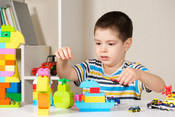 A handsome boy of 4 years old plays with cars and a construction set, games of preschool children, development of imagination.