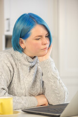 Focused student with dyed blue hair looking in laptop screen and pondering about problem solution....