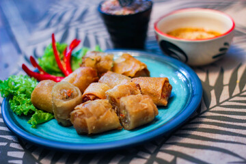 Deep fried spring rolls in blue plates with vegetables, chili and dipping sauce (Chinese food)