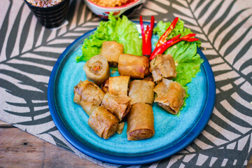 Deep fried spring rolls in blue plates with vegetables, chili and dipping sauce (Chinese food)