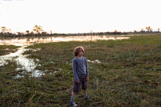 A Boy Standing Alone In An Inland Delta Landscape At Sunset. 