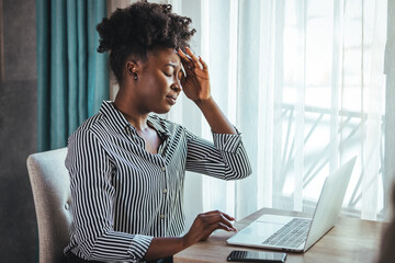 Young frustrated woman working at desk in front of laptop suffering from chronic daily headaches, treatment online, appointing to a medical consultation, electromagnetic radiation, sick pay