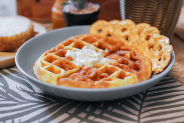 Waffles topped with honey in a gray plate with bread and seasonings placed on a wooden table.