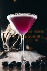 Smoking martini glass with purple drink. Cocktail with blueberries 