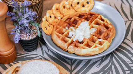 Waffles topped with honey in a gray plate with bread and seasonings placed on a wooden table.