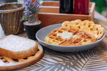 Waffles topped with honey in a gray plate with bread and seasonings placed on a wooden table.