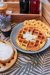 Waffles topped with honey in a gray plate with bread and seasonings placed on a wooden table.