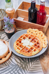 Waffles topped with honey in a gray plate with bread and seasonings placed on a wooden table.
