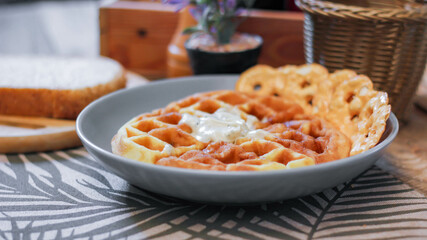 Waffles topped with honey in a gray plate with bread and seasonings placed on a wooden table.