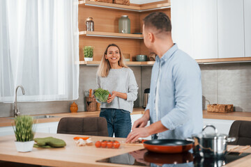 Man standing by the table. Couple preparing food at home on the modern kitchen