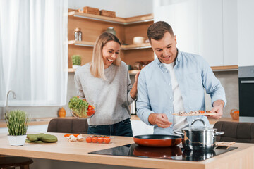 Man standing by the table. Couple preparing food at home on the modern kitchen