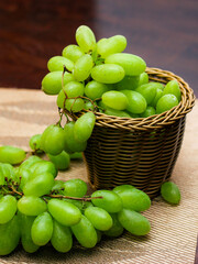 Green Grape placed in a woven basket and a wooden table top.