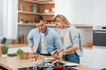Using vegetables. Couple preparing food at home on the modern kitchen