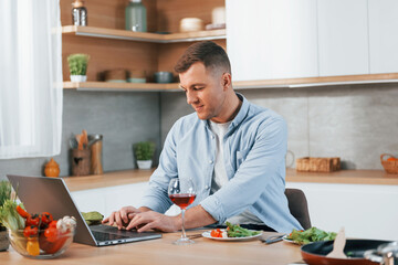 Using laptop. Man preparing food at home on the modern kitchen