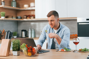 Obraz premium Using laptop. Man preparing food at home on the modern kitchen