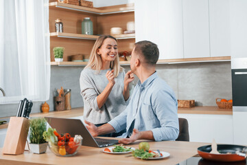 Laptop is on the table. Couple preparing food at home on the modern kitchen