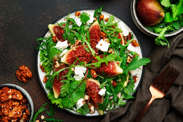 Summer salad with figs, white cheese, walnuts, chard and arugula with jam dressing on brown background, top view, copy space