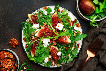 Summer salad with figs, white cheese, walnuts, chard and arugula with jam dressing on brown background, top view, copy space