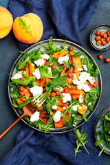 Summer salad with grilled peach with soft cheese, hazelnuts and arugula on blue table background, top view, copy space