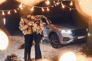 With warm drinks. Couple standing in the forest and celebrating New year