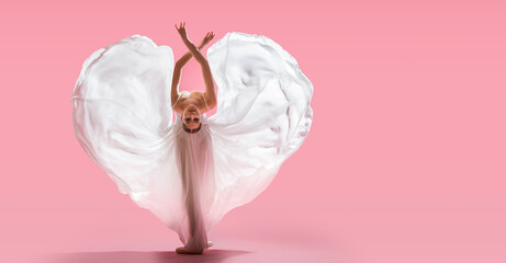 elegant ballerina in pointe shoes dancing in a long white skirt developing in the shape of a heart on a pink background - obrazy, fototapety, plakaty