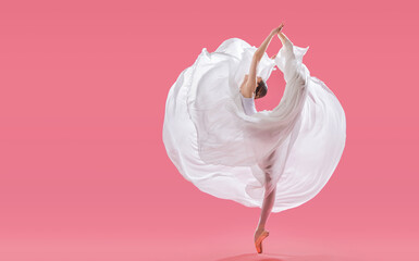 elegant ballerina in pointe shoes dancing in a long white skirt on a pink background