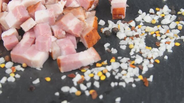 Meat delicacy. Sliced bacon cubes, basil and seasonings on a rotating slate tray. Macro