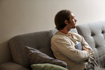 Obraz premium Ginger bristle man looking aside while sitting with book on couch