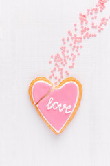 Broken heart shaped cookie with text LOVE is falling down like a comet, top view, flat lay