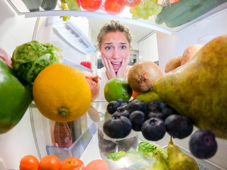 Young woman scared looking at healthy food inside the frigde