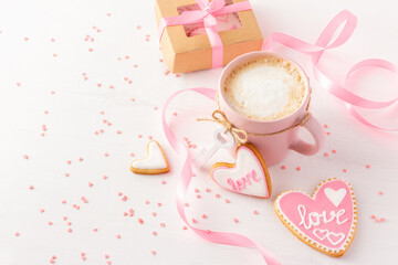 Valentine day breakfast with coffee and heart shaped cookies on white background decorated with pink ribbons and sweet prinkles.
