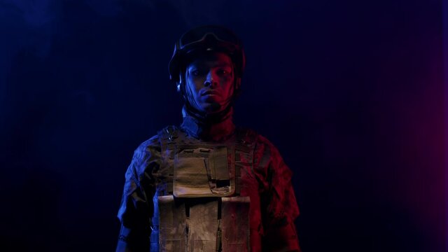 Serious soldier man in military uniform lowers, raises weapon with hands, looking at the camera and standing in the studio with gradient light. Concept of military uniforms and army.