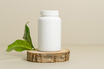 White bottle for medical pills or vitamins on wooden stand with green leaves, organic herbal...