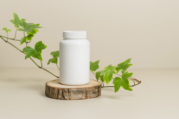 White medicine mockup bottle for vitamins or pills on wooden podium with green plant leaves at the...