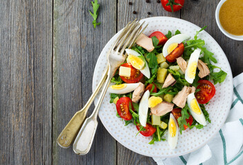 Set of raw ingredients potatoes, eggs, fresh arugula, olive oil, pepper, canned tuna, cherry tomatoes, salt to prepare a salad Nicoise on the old wooden background. Rustic style.Top view.