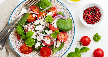 Tomatoes, spinach leaves, red onions and feta cheese salad on a light ceramic plate. Selective focus. Top view.