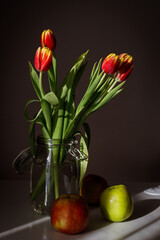 Red tulips stand in a jar on a white table in the sunlight