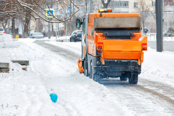 A sweeper moves along a snow-covered street and cleans the snow on a paved sidewalk.