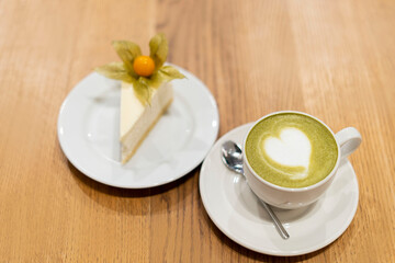 Close-up of a cup with a matcha and a piece of cheesecake on a wooden table