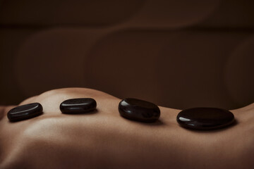 Woman getting spa treatment. Hot stone therapy. Side view. Brown color 