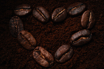 Kind of heart-shaped coffee beans lie on ground coffee. View from above. Flat lei. Love for coffee drink. Back for coffee shop or restaurant