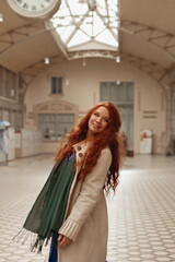 Fototapeta premium portrait of red-haired young woman in a light coat at the train station smiles, selective focus